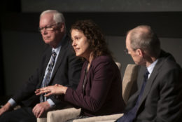 woman speaking seated in between two men on stage