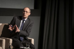 man speaking with his hands out wearing a suit on stage