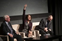 woman with her arm raised and a smile in between two men on stage