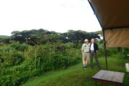 two men posing next to tent and field of green and trees