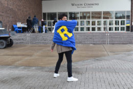 the back of a male student wearing blue cape and a yellow R in front of wilson commons stairs