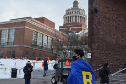 the back of a male student wearing blue cape and a yellow R and rush rhees library tower in background