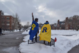 two people wearing R capes standing on bench in quad covered in snow