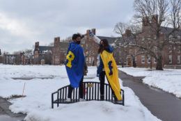 two people wearing R capes standing on bench in quad covered in snow