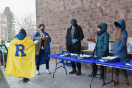 brick background with table with blue cloth and t-shirts piled on and a group of students