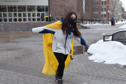 woman facing camera wearing a yellow cape long dark hair and a dark blue mask