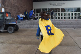woman walking away wearing large yellow cape and blue large R on it in front of staircase