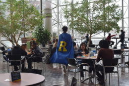 man in blue cape and yellow R on the back walking through wilson commons