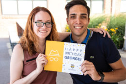 man and woman posing for photo holding happy birthday george sign