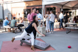 a woman playing cornhole with party in background
