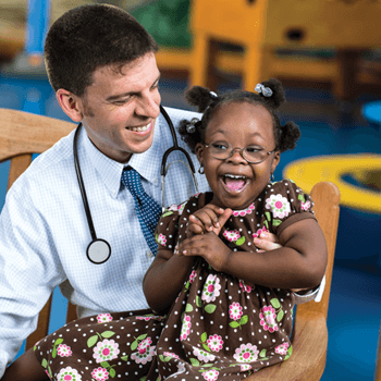 a male doctor holds a female child in a room.