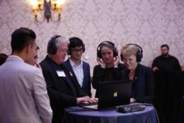 four people in headphones looking at laptop viewing a demo