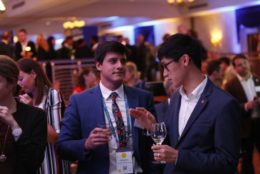 two man in suits speaking with drinks in their hand at an event