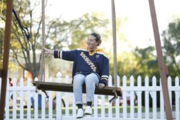 Ethan Okoshi sitting on giant swing in quad wearing rochester hockey sweatshirt