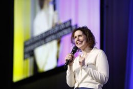 woman on stage holding a mic giving a talk or performance