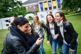 five woman in quad laughing in front of giant meliora letters