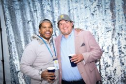 two men wearing hats and holding a cup posing in photo booth