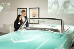 man and woman looking at a light green classic convertible