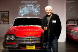 man holding a bottle smiling for photo with bright red vintage car in background