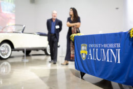 man and woman in background with blue rochester alumni banner in foreground