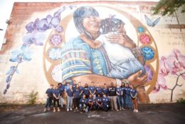 large group of volunteers in front of mural posing for photo wearing matching blue alumni tshirts