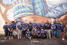 large group of volunteers in front of mural posing for photo wearing matching blue alumni tshirts