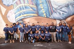 large group of volunteers in front of mural posing for photo wearing matching blue alumni tshirts