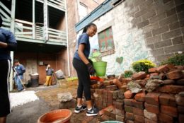 woman holding green pot in front of a pile of bricks