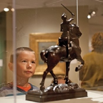 a child stares into a case which holds a figurine of a soldier on a horse.