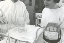 1970 black/white photo in NICU of a baby and man and woman standing over