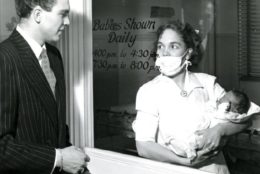 black/white photo from 1947 woman holding a baby in nursery to a man outside the glass
