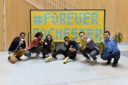 six students squatting for photo with #Forever Rochester banner behind them