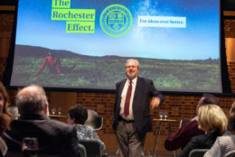 man in suit and tie with beard and glasses speaking on stage