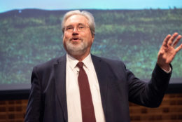 man in suit and tie with beard and glasses speaking on stage