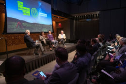 four speakers on stage with large screen behind them