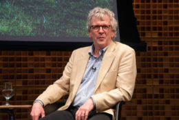 man seated with tan sport jacket and glasses looking at camera