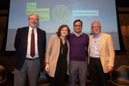 three men and a woman smiling for photo with large screen in background