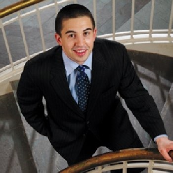 a young man dressed in a suit poses for a picture within a staircase.
