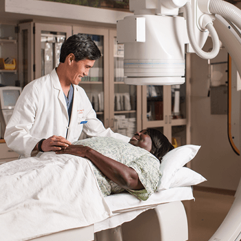 a doctor and a patient are smiling at each other as the patient lies on a table within a medical office.