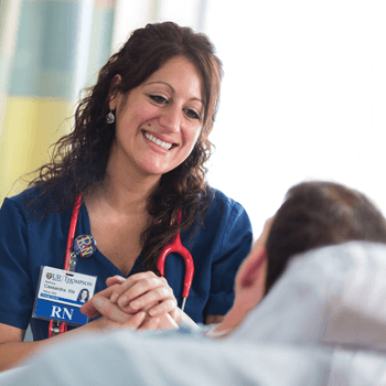 a registered nurse comforts a patient as they lie on their bed.