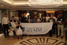 group of people holding a rochester alumni banner at an event