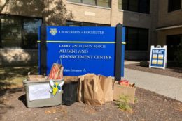 blue U of R sign for the alumni center with bags and bins in front of it