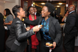 two woman in a crowd embracing each other with food and drink in hand