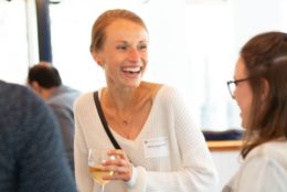 woman with smile holding glass of wine speaking to a friend an an event