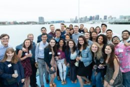 large group of young alumni posing in front of harbor and city background
