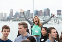 woman with large smile and arms in air posing for photo in a group in front of harbor and city background