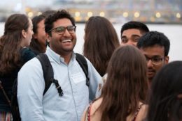 man with glasses and backpack smiling speaking with a group of friends at an event