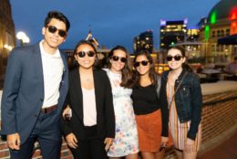 four woman one man wearing sunglasses posing for photo with city in background