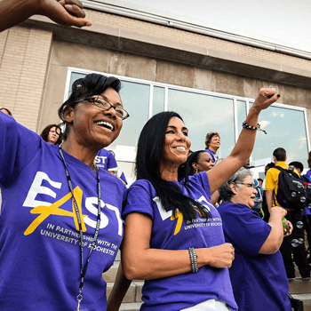 a group of staff and students cheer as they are all grouped outside together for an event.