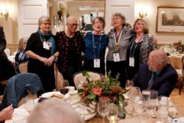 five woman standing and singing at an event in front of dinner table